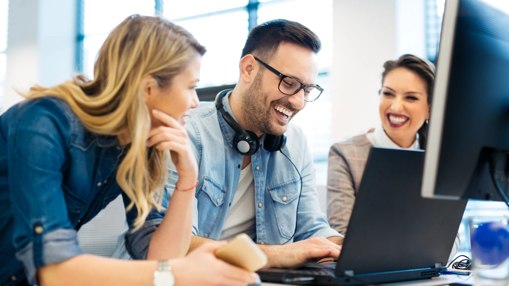 co-workers huddle around a laptop discussing how they can use automated software to make their small business run smoothly
