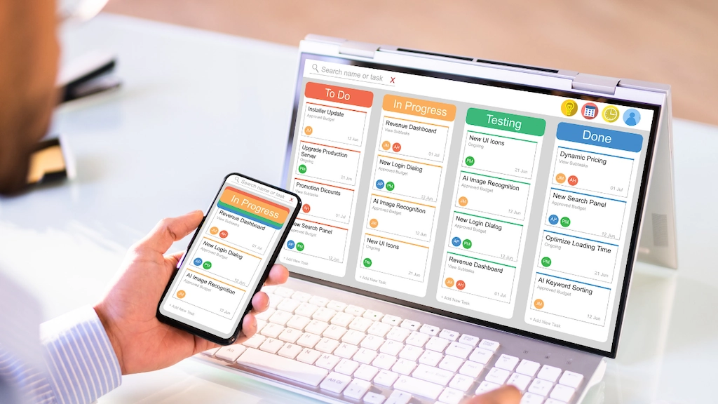 picture of a person holding a smartphone with their laptop open to a software dashboard filled with data on the screen